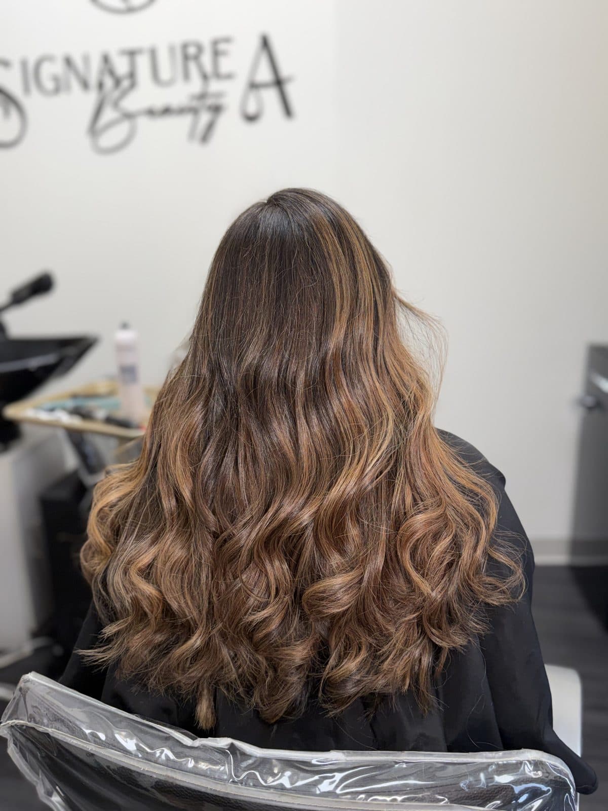 Warm balayage on long wavy brunette hair, seen from behind